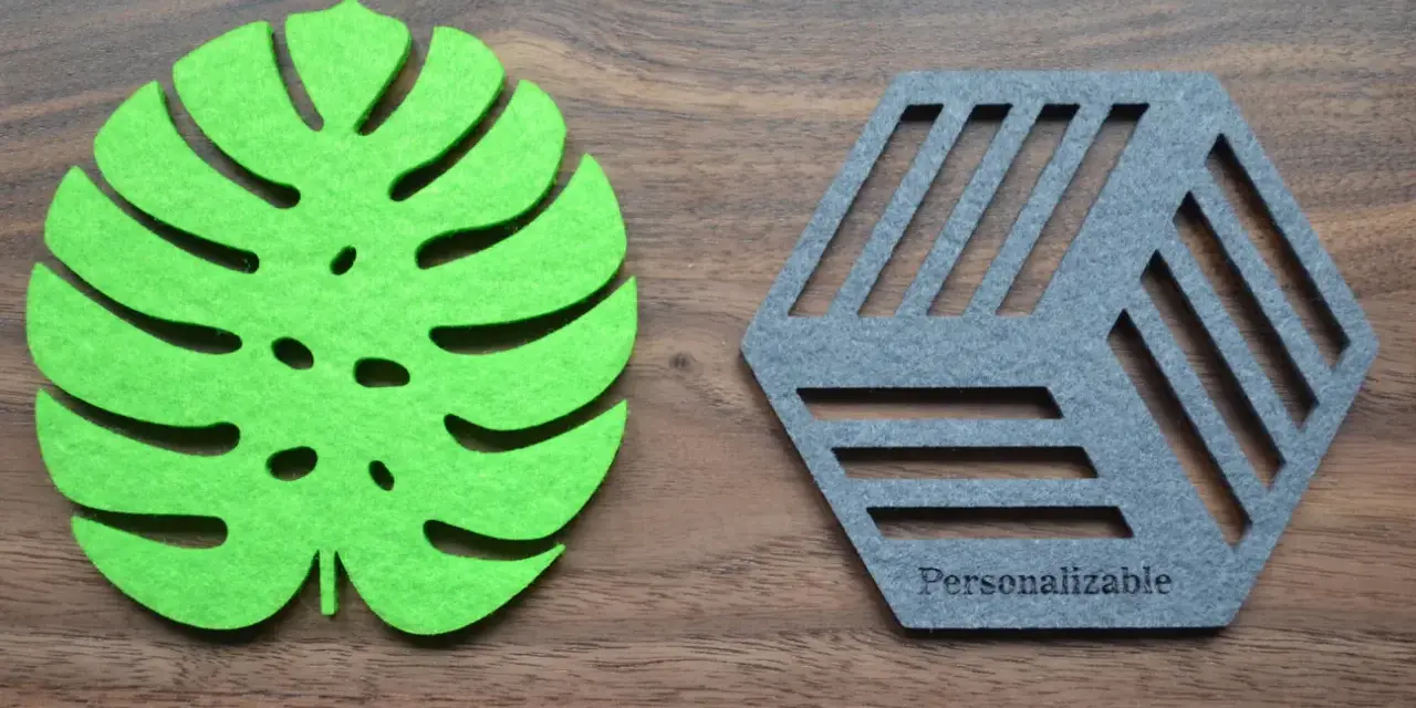 Posavasos de fieltro verde con forma de hoja y otro gris hexagonal con líneas, sobre fondo de madera.