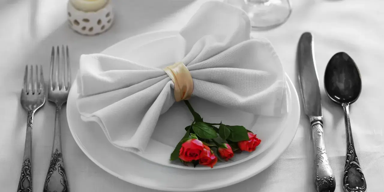 Mesa elegante: tenedor a la izquierda, cuchillo y cuchara a la derecha. Servilleta con rosas, ideal para saber como colocar los cubiertos en la mesa.