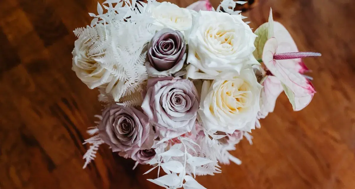 Un ramo de novia con rosas blancas y lilas, helechos blancos y una flor de anthurium rosa. Un recuerdo para secar y atesorar.