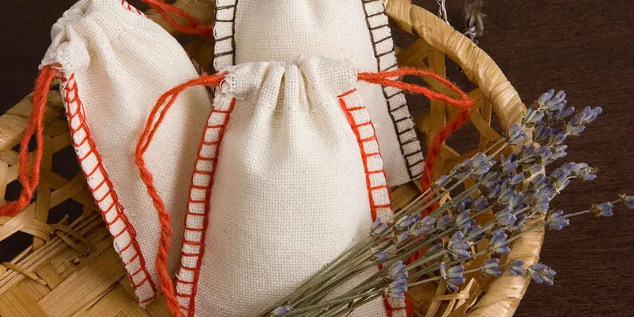 Bolsitas perfumadas para armarios caseras, hechas a mano con tela de lino y cordones rojos, junto a un manojo de lavanda seca en una cesta de mimbre.