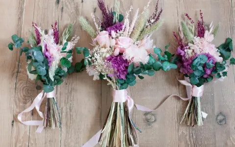 Tres ramos de flores secas y eucalipto, atados con cintas rosas. Un detalle que regala la madrina de boda a los novios.