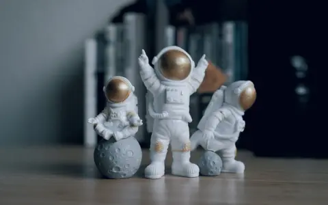 Tres figuras de un disfraz astronauta casero, una meditando sobre la luna, otra celebrando y la tercera jugando con una pequeña luna.