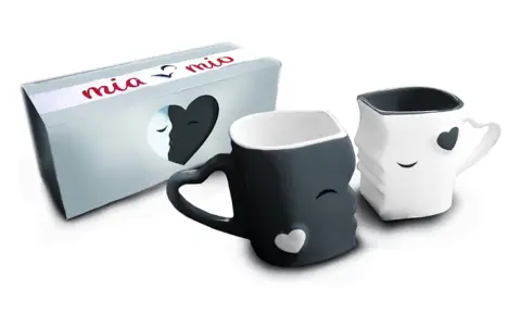 Dos tazas de amor, una negra y otra blanca, con forma de rostros que se miran. La caja dice "mia & mio".