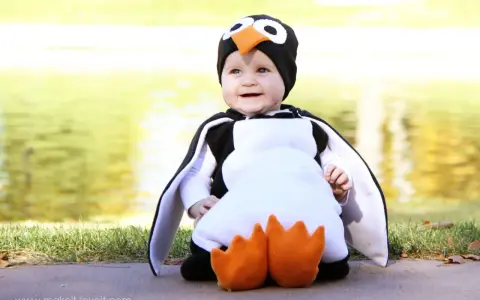 Bebé sonriente con un adorable disfraz pinguino casero, con aletas y pico naranja.