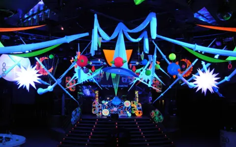 Decoración vibrante para una fiesta futurista, con luces neón, telas colgantes y estructuras geométricas que crean un ambiente de otro mundo.