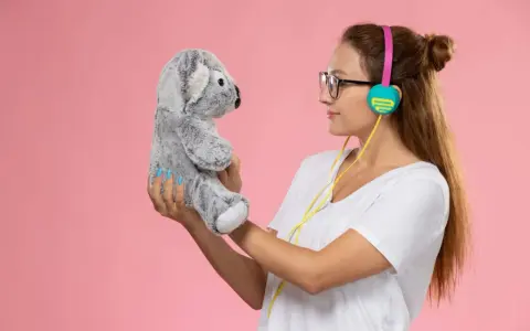 Mujer con auriculares sostiene un peluche de koala gris, como si compartieran secretos. ¡Un par de osos personalizados para la diversión!