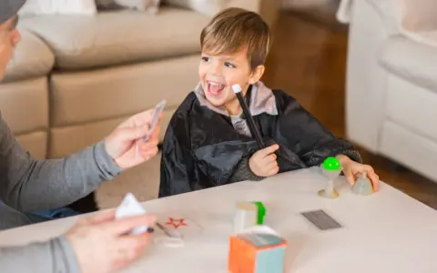 Niño con túnica de mago practica trucos de magia para niños con las manos, usando varita y cartas.