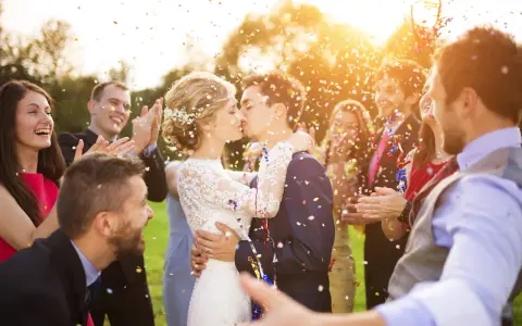 Novios besándose entre confeti mientras amigos aplauden y ríen. ¡Un momento perfecto para felicitar a unos novios!