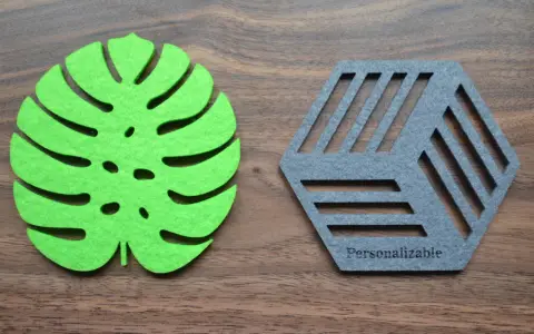 Posavasos de fieltro verde con forma de hoja y otro gris hexagonal con líneas, sobre fondo de madera.