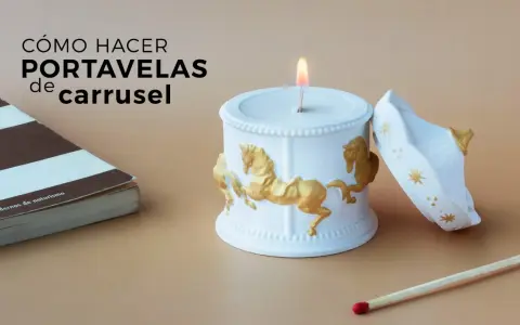 Portavelas manualidades de carrusel, blanco con caballos dorados, junto a un libro y una cerilla.
