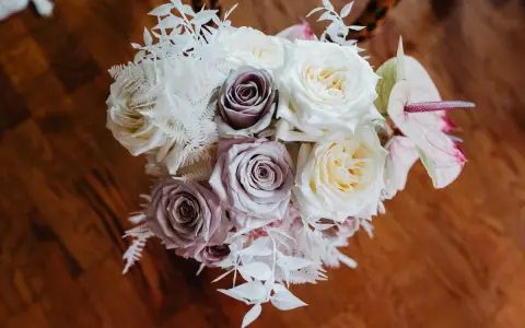 Un ramo de novia con rosas blancas y lilas, helechos blancos y una flor de anthurium rosa. Un recuerdo para secar y atesorar.