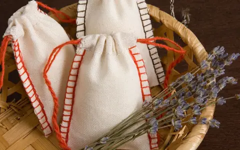 Bolsitas perfumadas para armarios caseras, hechas a mano con tela de lino y cordones rojos, junto a un manojo de lavanda seca en una cesta de mimbre.