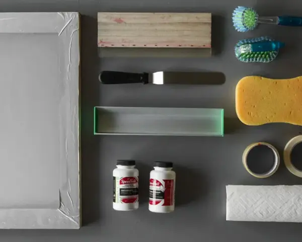 Marco de serigrafía, rasquetas, esponja, cintas, papel, cepillos y tubos de pintura acrílica, todo listo para empezar con los materiales serigrafia.