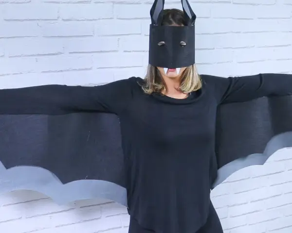 Persona con un disfraz murciélago casero, alas negras y máscara con colmillos.