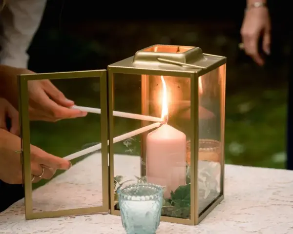 Manos encienden velas finas de una vela principal dentro de un farol dorado. Una escena de la ceremonia de las velas.