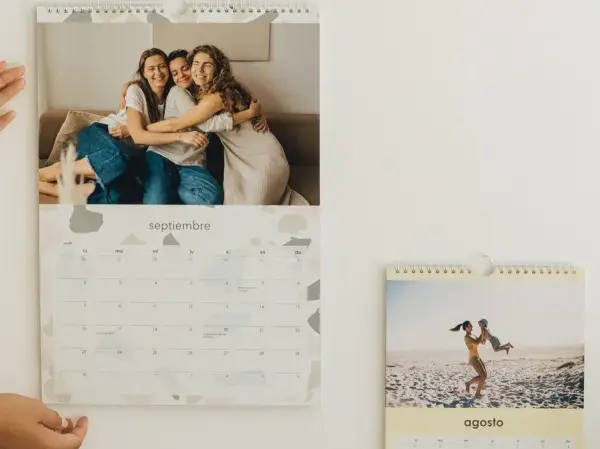 Un calendario personalizado con fotos de amigos y familia. El mes de septiembre muestra a tres amigas abrazándose, y agosto a una madre jugando con su hijo en la playa.
