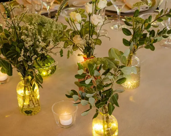 Elegante decoracion con velas y flores en jarrones de cristal, creando un ambiente cálido y acogedor para una cena especial.