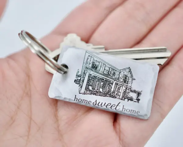 Un llavero hogar con la imagen de una casa y la frase "home sweet home" descansa en una mano.