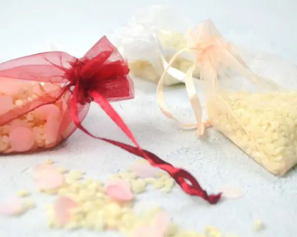 Bolsitas de organza rojas, blancas y melocotón llenas de arroz, listas para usarse como recuerdo. Ideas para como hacer bolsitas de arroz para bodas.