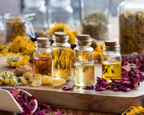 Botellas con aceites esenciales y pétalos de rosa, manzanilla y caléndula. Ideas para saber como hacer esencias aromaticas caseras.