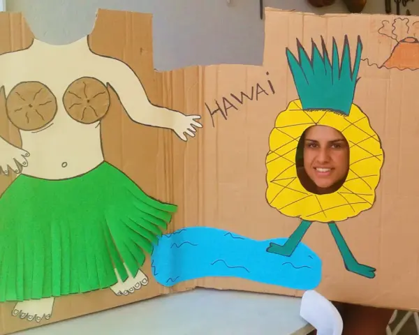 Divertido photocall hawaiano casero con una figura de bailarina y una piña con cara sonriente. ¡Perfecto para unas fotos tropicales!