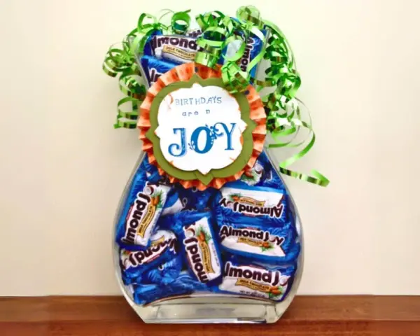 Un jarrón lleno de botes de chuches caseros, decorado con un lazo verde y un mensaje que dice "BIRTHDAYS are a JOY".