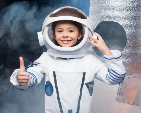 Niña sonriente con un disfraz de universo casero de astronauta, pulgar arriba, lista para explorar.
