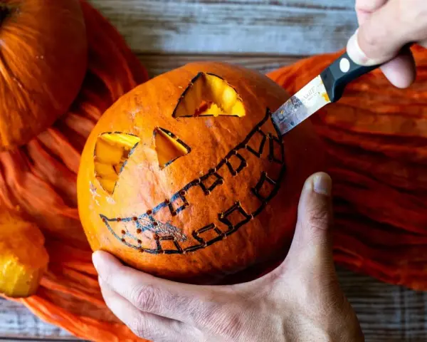Creando una calabaza de Halloween fácil. Un cuchillo talla una sonrisa dentada en una calabaza naranja, con ojos triangulares ya cortados.