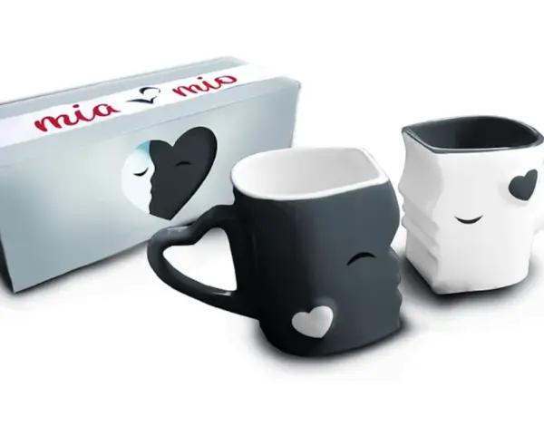 Dos tazas de amor, una negra y otra blanca, con forma de rostros que se miran. La caja dice "mia & mio".