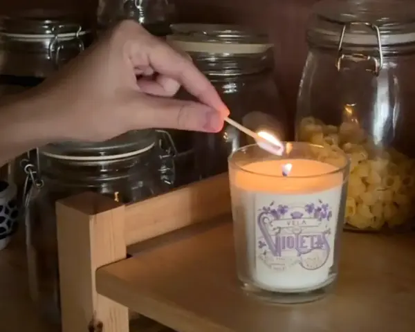 Encendiendo una vela decorada, parte de manualidades para decorar velas, con frascos de vidrio de fondo.