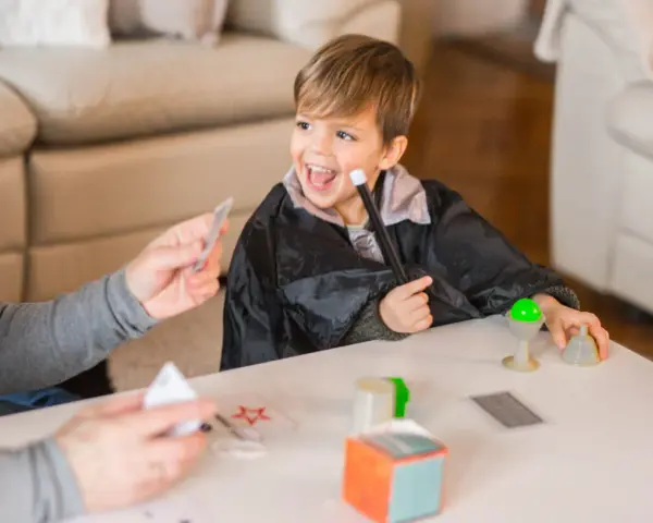 Niño con túnica de mago practica trucos de magia para niños con las manos, usando varita y cartas.