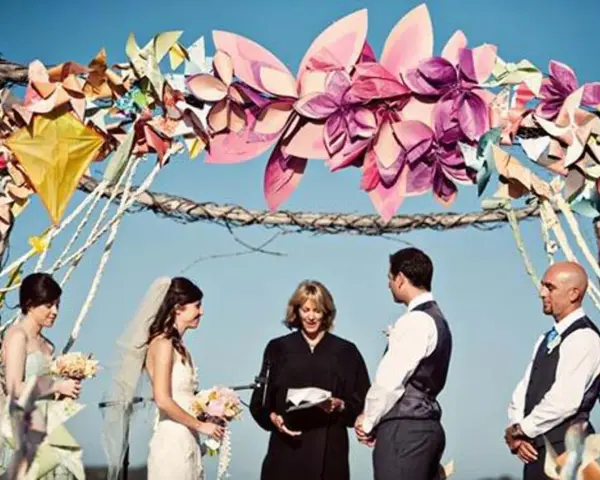 Boda al aire libre con un arco decorado con manualidades de papel coloridas. La pareja se da el sí ante un oficiante.