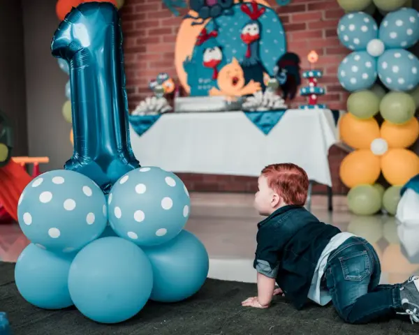 Niño gateando junto a globos azules y un gran número 1. Ideas para como preparar una fiesta infantil barata y muy original.