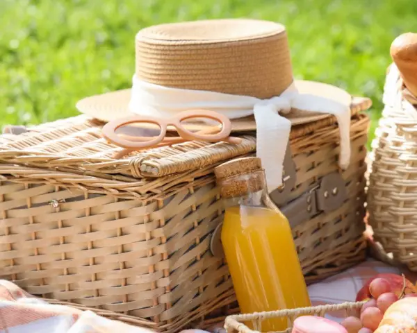Cajas picnic listas para disfrutar: sombrero, gafas de sol, jugo y frutas sobre mantas a cuadros en un día soleado.