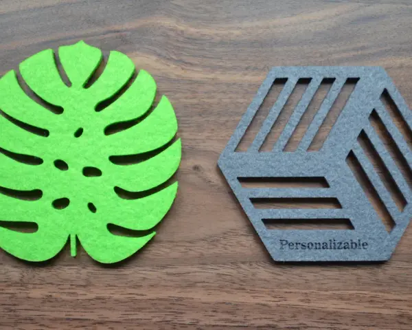 Posavasos de fieltro verde con forma de hoja y otro gris hexagonal con líneas, sobre fondo de madera.