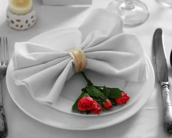 Mesa elegante: tenedor a la izquierda, cuchillo y cuchara a la derecha. Servilleta con rosas, ideal para saber como colocar los cubiertos en la mesa.