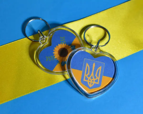 Dos llaveros en forma de corazón con la bandera de Ucrania. Uno tiene un girasol, el otro el escudo. Ideas para como hacer llaveros personalizados.