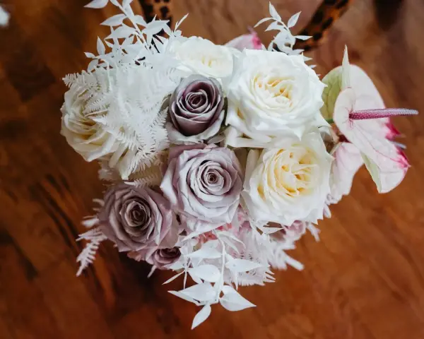 Un ramo de novia con rosas blancas y lilas, helechos blancos y una flor de anthurium rosa. Un recuerdo para secar y atesorar.