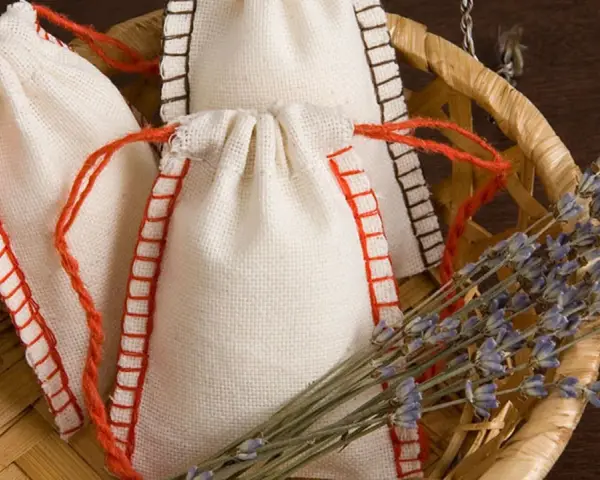 Bolsitas perfumadas para armarios caseras, hechas a mano con tela de lino y cordones rojos, junto a un manojo de lavanda seca en una cesta de mimbre.