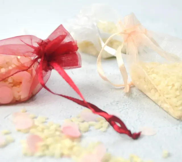 Bolsitas de organza rojas, blancas y melocotón llenas de arroz, listas para usarse como recuerdo. Ideas para como hacer bolsitas de arroz para bodas.