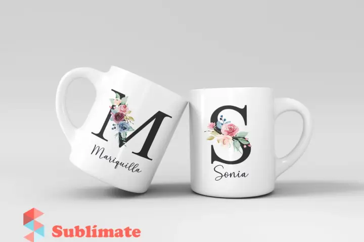 Dos tazas blancas con iniciales decoradas con flores. Una tiene la "M" de Mariquilla, la otra la "S" de Sonia.