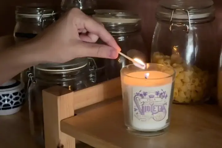 Encendiendo una vela decorada, parte de manualidades para decorar velas, con frascos de vidrio de fondo.