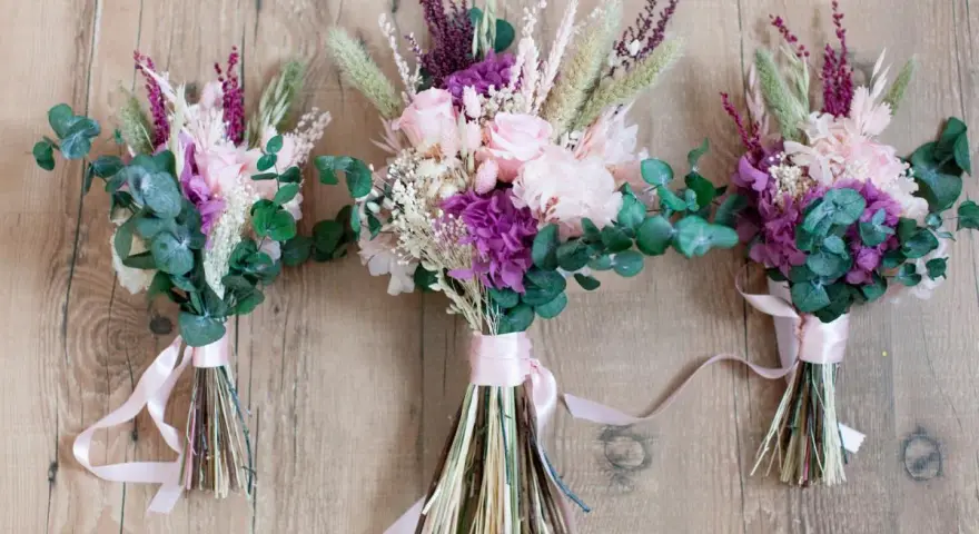 Tres ramos de flores secas y eucalipto, atados con cintas rosas. Un detalle que regala la madrina de boda a los novios.