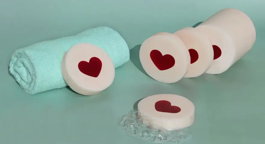 Jabones de glicerina con corazones rojos, listos para hacer jabón. Toalla turquesa y burbujas.