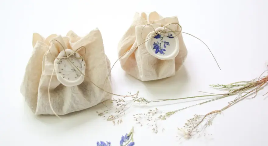 Dos pequeños paquetes de tela rústica, atados con hilo y sellados con cera, decorados con flores secas. Son detalles de boda originales hechos a mano, perfectos para un toque natural.
