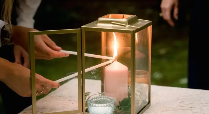 Manos encienden velas finas de una vela principal dentro de un farol dorado. Una escena de la ceremonia de las velas.