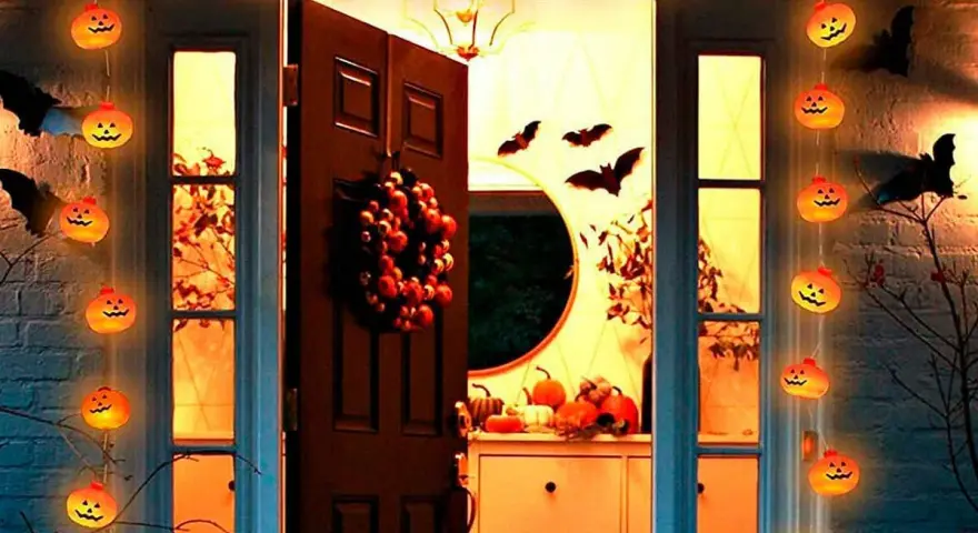Guirnalda de calabazas iluminadas y murciélagos de cartón crean una espeluznante decoración de terror casera frente a una puerta.