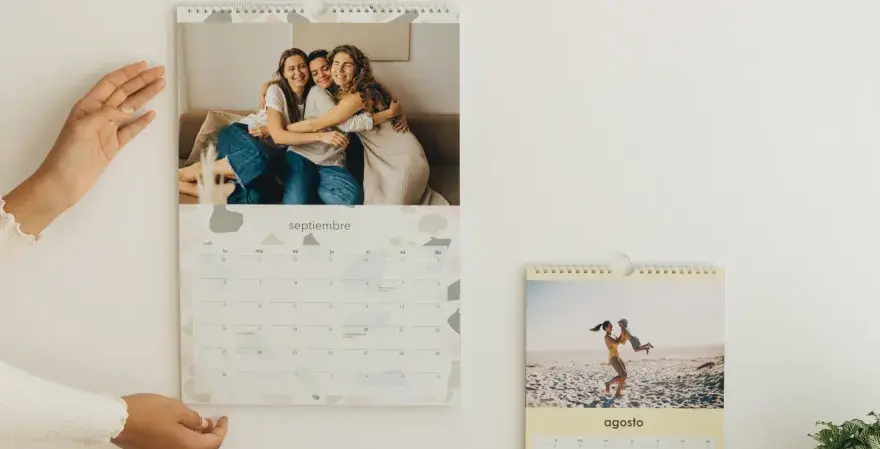 Un calendario personalizado con fotos de amigos y familia. El mes de septiembre muestra a tres amigas abrazándose, y agosto a una madre jugando con su hijo en la playa.