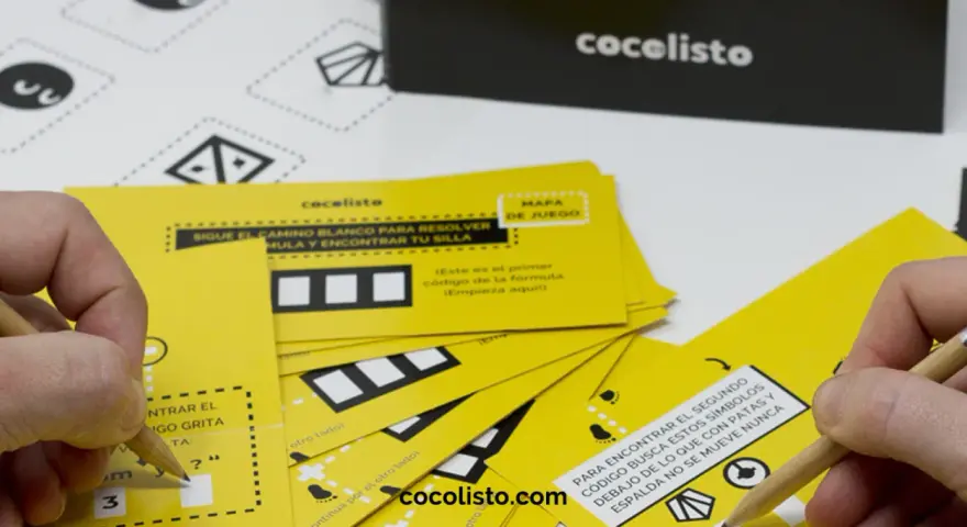 Manos resolviendo juegos para comida de empresa con tarjetas amarillas y lápices. ¡Diversión garantizada!