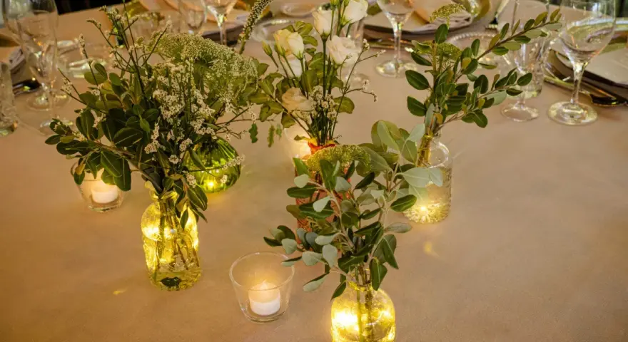 Elegante decoracion con velas y flores en jarrones de cristal, creando un ambiente cálido y acogedor para una cena especial.